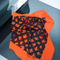 A silk scarf with orange edges and a black and orange pattern, displayed on a reflective surface.