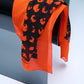 A luxury silk scarf in vibrant orange and black, featuring a bold abstract leopard-style print, elegantly draped over a modern curved glass chair.