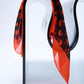 silk scarf in vibrant orange and black, featuring an abstract leopard-style print, elegantly draped over a modern curved glass chair in a bright studio.