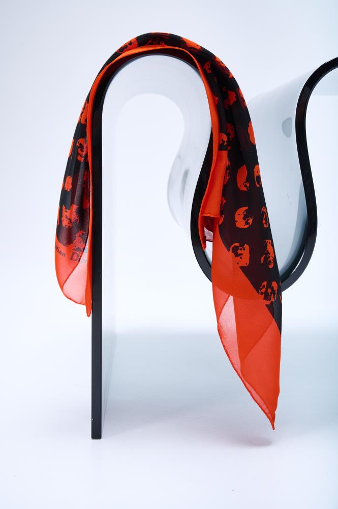 silk scarf in vibrant orange and black, featuring an abstract leopard-style print, elegantly draped over a modern curved glass chair in a bright studio.
