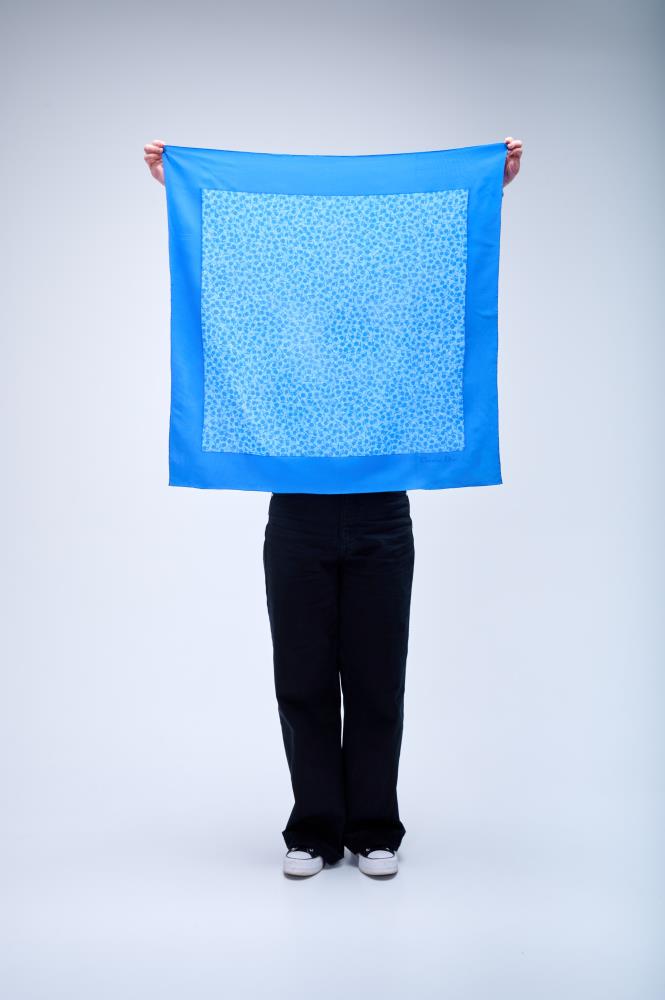 A person holding up a large square  silk scarf in vibrant sky blue, featuring a solid border and a delicate ditsy floral pattern in the center.