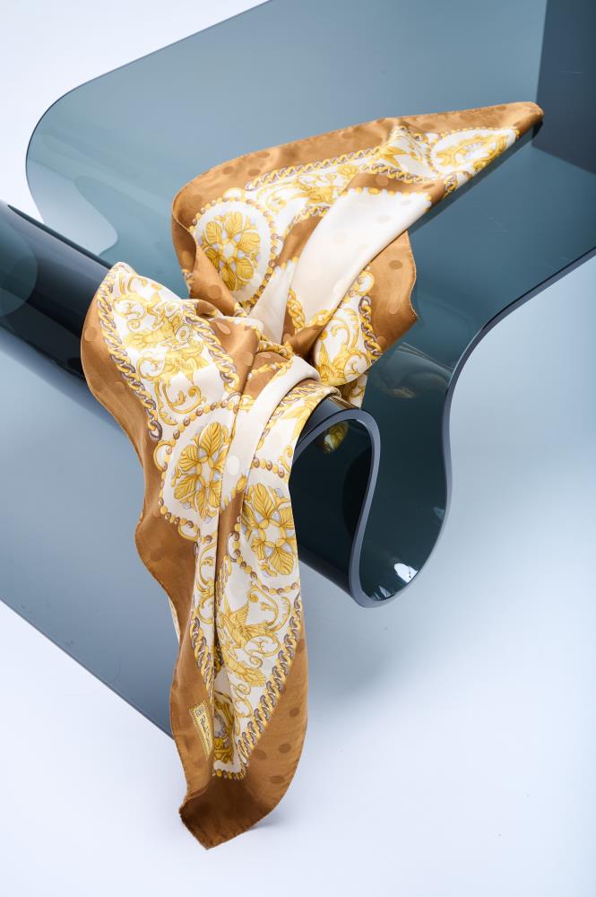 A vintage silk scarf in white, caramel, and brown with rolled and tucked edges, displayed on a glass surface.