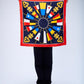 A person holding up a large square silk scarf with a nautical theme, featuring gold keys and maritime flags arranged in a sunburst pattern on a navy blue background with a red border.