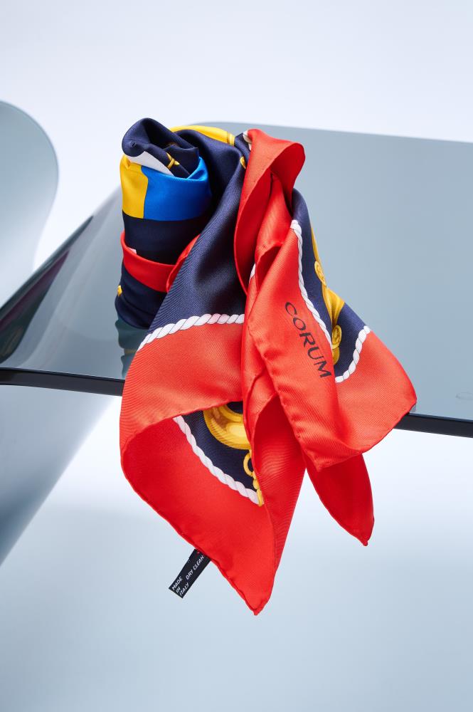 silk scarf with a nautical theme, featuring vibrant red and navy blue panels with white rope details, artfully draped on a glass surface.
