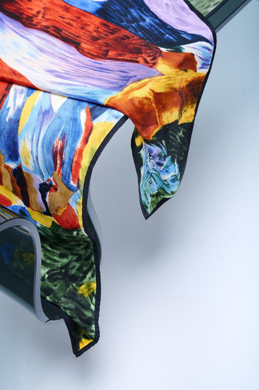 A multicolored silk scarf with a vibrant pattern, displayed on a surface with its ends fanned out.