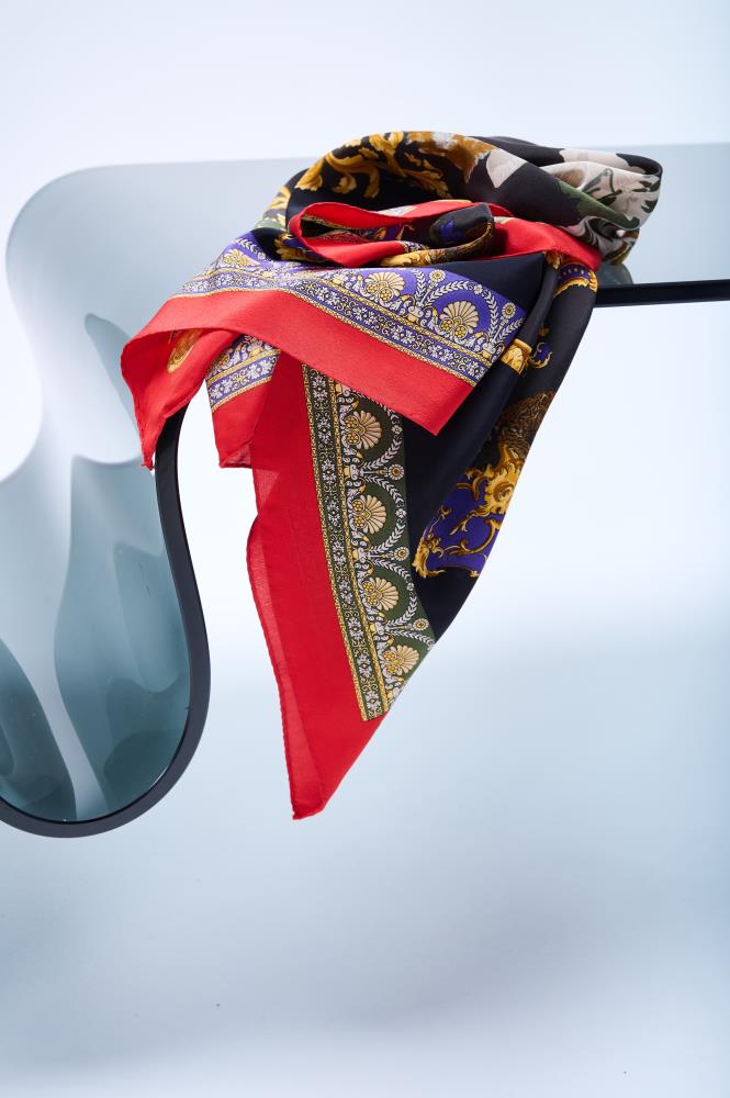 A vintage silk scarf with red edges, featuring lions and cheetahs, displayed on a surface.