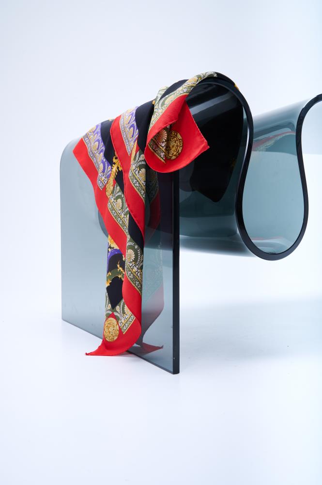 Luxury silk scarf with a baroque-style pattern and a vibrant red border, elegantly draped over a modern, curved translucent chair in a white studio setting.