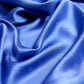 Extreme close-up of a royal blue silk scarf featuring a subtle embossed monogram pattern, highlighting the luxurious fabric drapes and glossy sheen