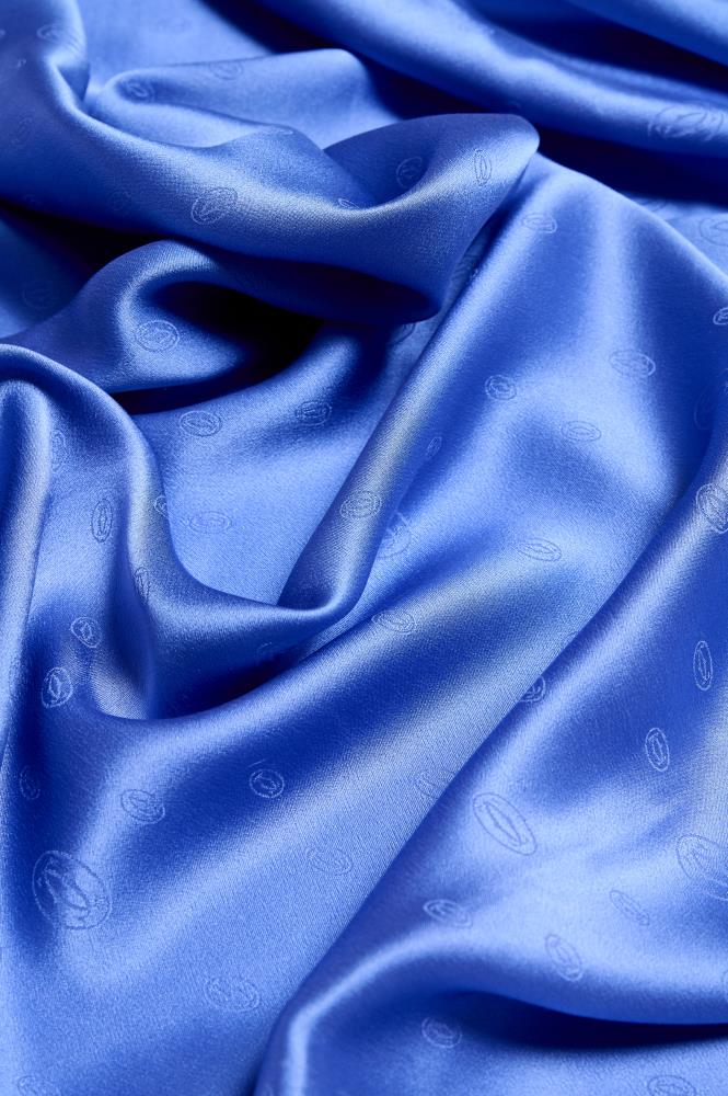 Extreme close-up of a royal blue silk scarf featuring a subtle embossed monogram pattern, highlighting the luxurious fabric drapes and glossy sheen