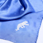 A close-up of a luxuriously draped royal blue silk scarf featuring a subtle monogram pattern and a detailed white panther embroidery on the corner.