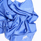 Artfully draped royal blue silk scarf on a white background, featuring a subtle monogram pattern and a distinct white embroidered panther motif in the bottom corner.