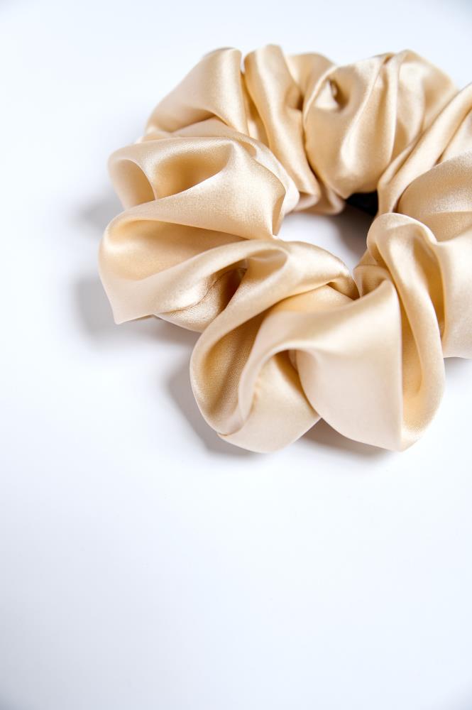 Close up of a single beige satin silk scrunchie on a light background.