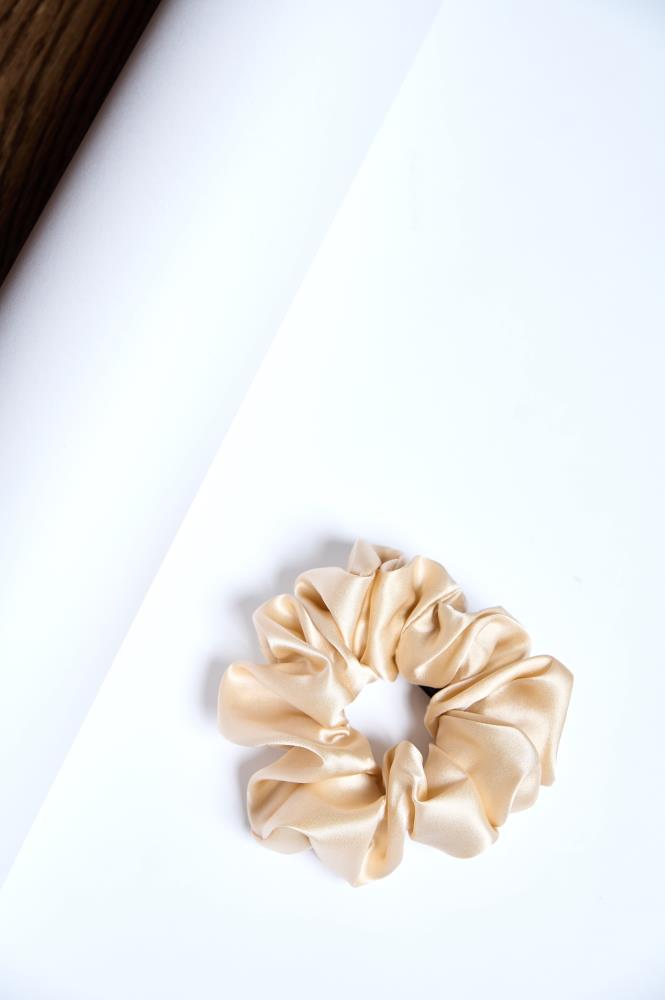 A beige silk scrunchie placed on a white surface.