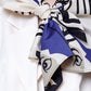 A close-up of a person wearing a white blazer and an abstract patterned scarf in blue, cream, and black, tied in a large, elegant bow at the neck.