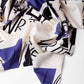 Folded fabric with bold, abstract black and blue geometric patterns and scattered letters on a white background. The design is modern and artistic.