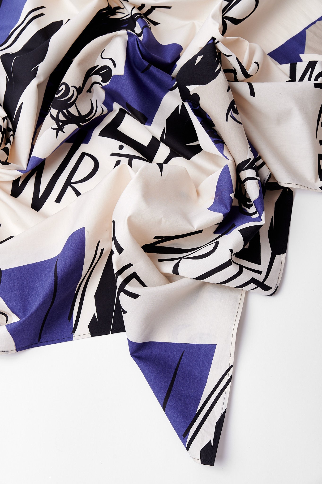 Folded fabric with bold, abstract black and blue geometric patterns and scattered letters on a white background. The design is modern and artistic.