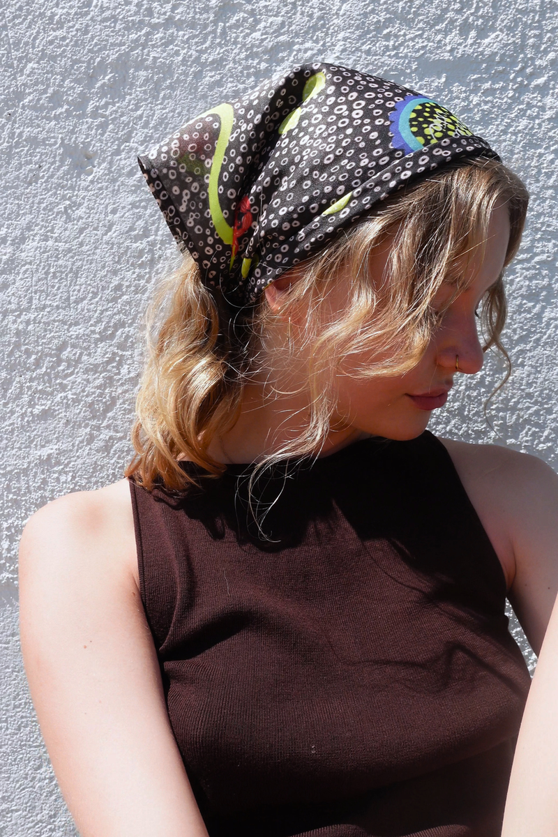 SKARELE Summer La Dolce Vita dark brown bandana headscarf with vibrant olive green and blue abstract pattern, styled on a blonde woman outdoors