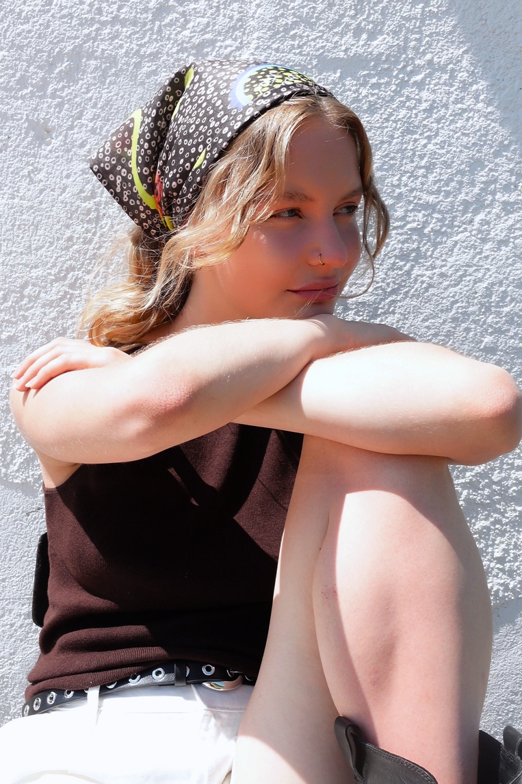 SKARELE "la dolce vita" brown bandana  with yellow and blue abstract dot pattern, worn by a young woman in bright sunlight against a textured wall