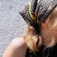 Close-up shot of SKARELE "Summer La Dolce Vita" dark brown silk blend headscarf with vibrant green and blue abstract pattern, tied as a bandana on a blonde woman.