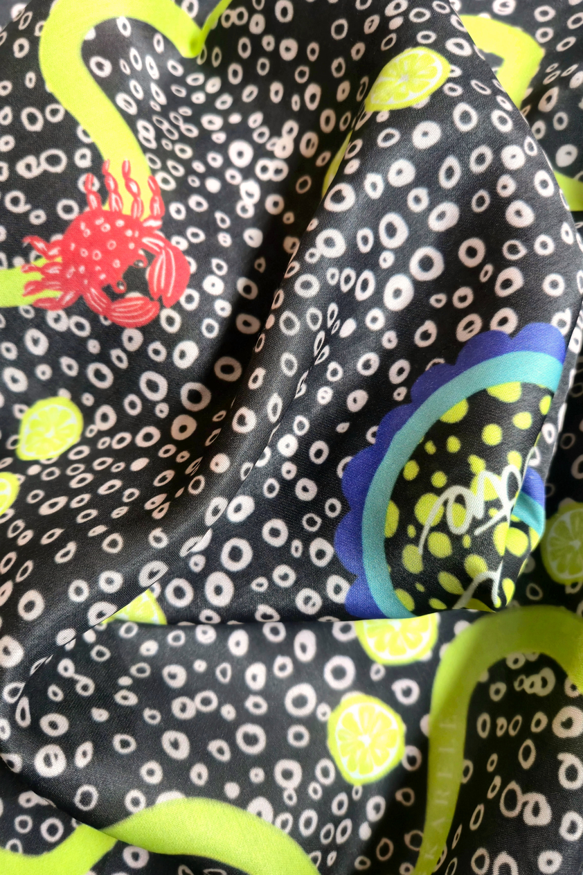 Detailed macro view of SKARELE "Summer La Dolce Vita" dark brown silk blend scarf fabric, featuring a red crab, lemon slices, and abstract polka dot print