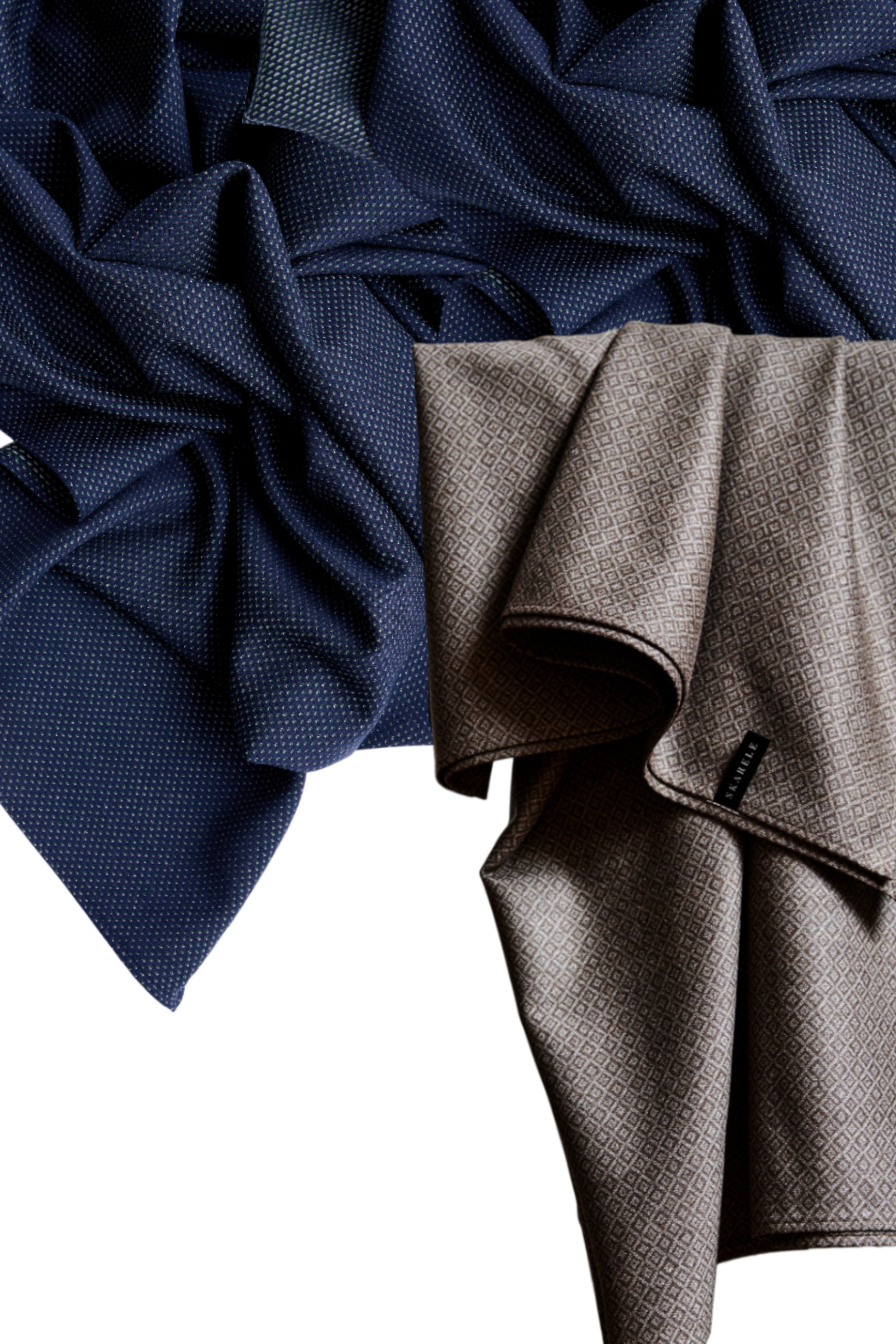 Two premium wool maxi scarves draped on a white background: one in deep navy blue with a fine gold dot pattern, and another in taupe with a subtle geometric diamond print.