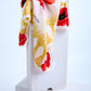Escada scarf featuring a vibrant red poppy floral print and yellow tassel motifs, artfully draped over a white stone pillar in a minimalist studio setting.
