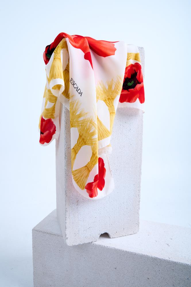 Escada scarf featuring a vibrant red poppy floral print and yellow tassel motifs, artfully draped over a white stone pillar in a minimalist studio setting.