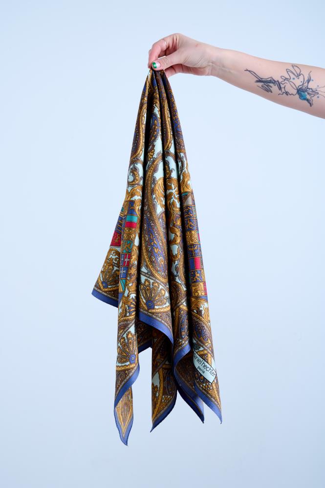 A multicolored silk scarf with a kaleidoscopic pattern, held up against a light background.