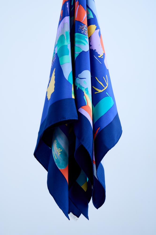 A vintage navy blue silk scarf featuring a vibrant abstract art print with colorful fish and coral motifs in orange, yellow, and turquoise, elegantly draped to showcase the fluid fabric
