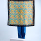 A silk scarf with a vibrant geometric pattern in black, blue, and yellow, draped over a stand against a white background.