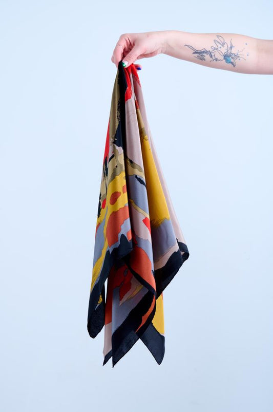 A multicolored silk scarf with geometric patterns, held up against a light background.