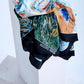 Close-up display of an artistic designer scarf with a masterpiece painting motif, showcasing the high-quality silk fabric's soft drape and detailed print against a minimalist studio background.