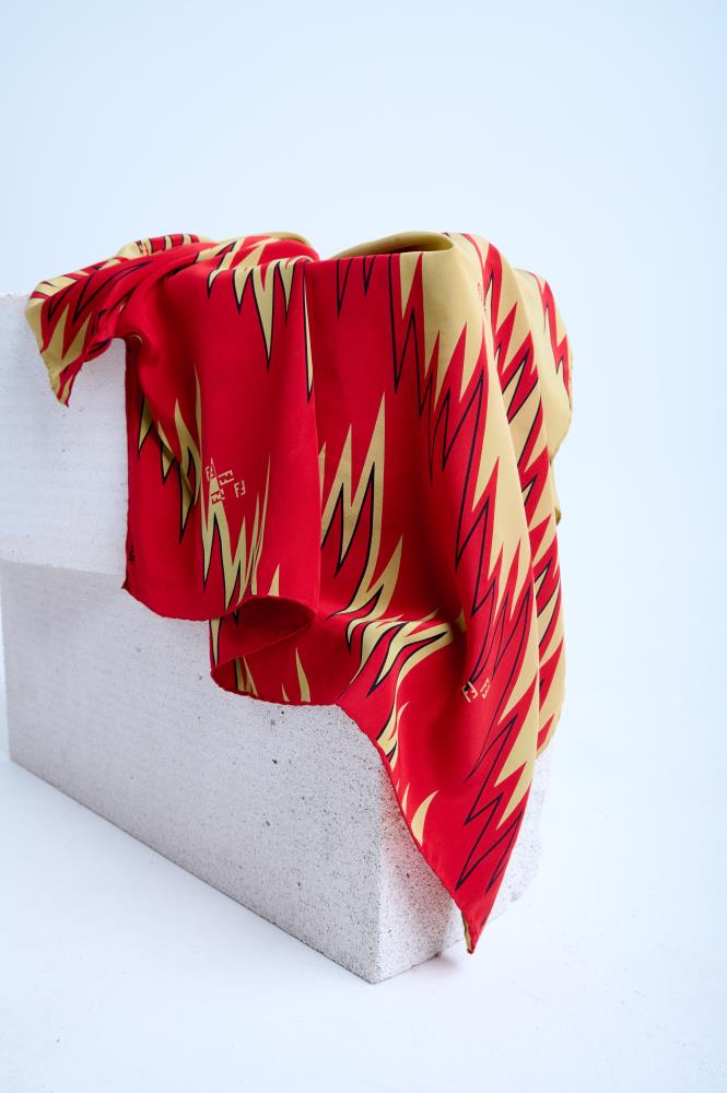 Close-up display of a luxury Fendi designer silk s scarf showcasing its iconic FF logo and distinctive geometric print, contrasted against a minimalist concrete surface to highlight the soft fabric drape.