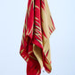 A vintage silk scarf in red and caramel colors with rolled and tucked edges, hanging against a white background.