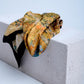A luxury silk scarf featuring a vibrant Impressionist-style painting print with rich yellow, orange, and blue tones, elegantly draped over a textured white concrete block.