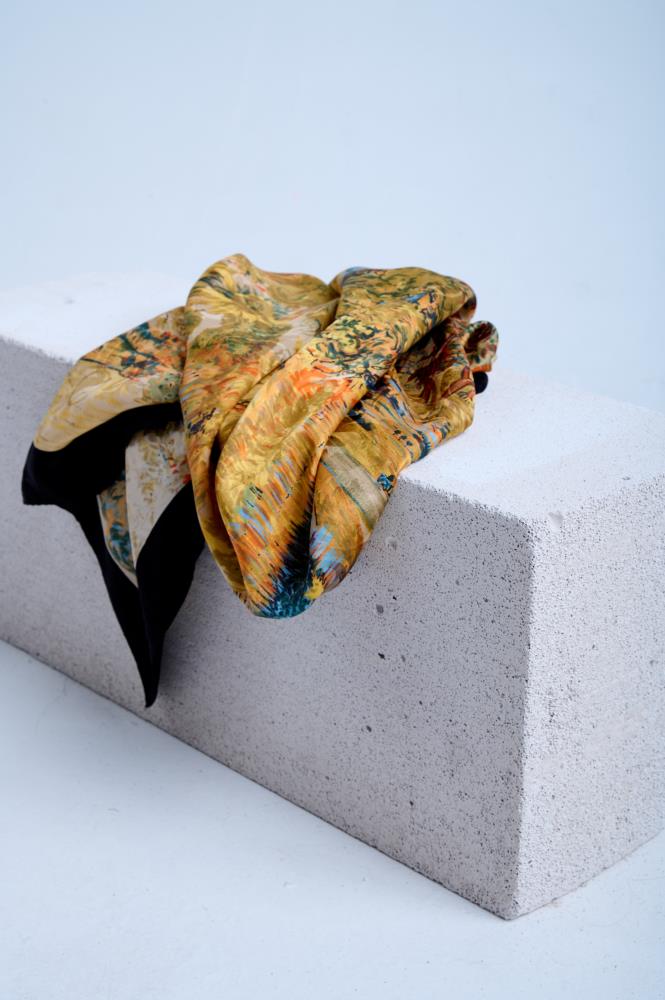 A luxury silk scarf featuring a vibrant Impressionist-style painting print with rich yellow, orange, and blue tones, elegantly draped over a textured white concrete block.