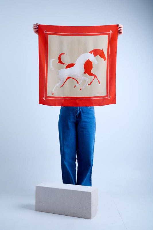 A person holding a red and beige silk scarf with a horse design against a white background, displaying the vintage scarf to a photographer.