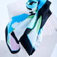 silk scarf with an abstract artistic print in pastel blue, pink, and green, featuring a bold black border, artfully rolled and draped on a white stone pedestal.