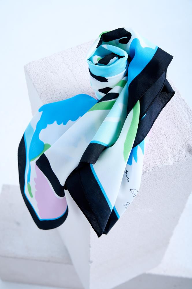 silk scarf with an abstract artistic print in pastel blue, pink, and green, featuring a bold black border, artfully rolled and draped on a white stone pedestal.