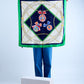 A person holding a vintage silk scarf with green and deep blue details, featuring rolled and tucked edges.