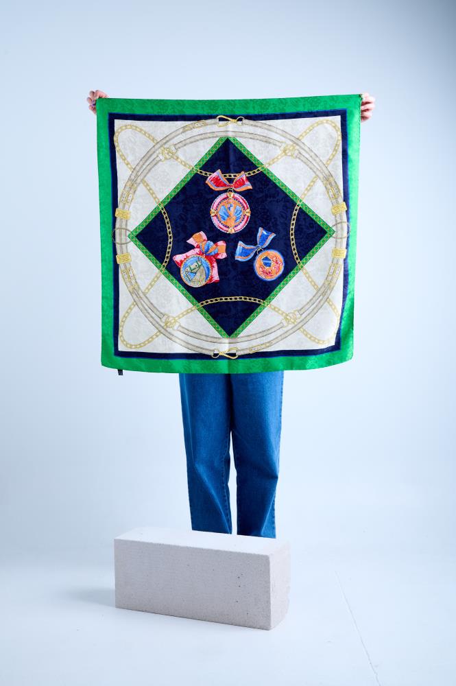A person holding a vintage silk scarf with green and deep blue details, featuring rolled and tucked edges.