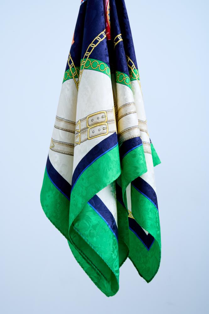 Close-up of a high-quality silk scarf with a nautical and equestrian theme, featuring golden chains and leather belts on a navy blue, white, and emerald green background.