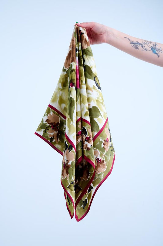 A person holding a silk scarf with a large floral pattern in shades of green and red.