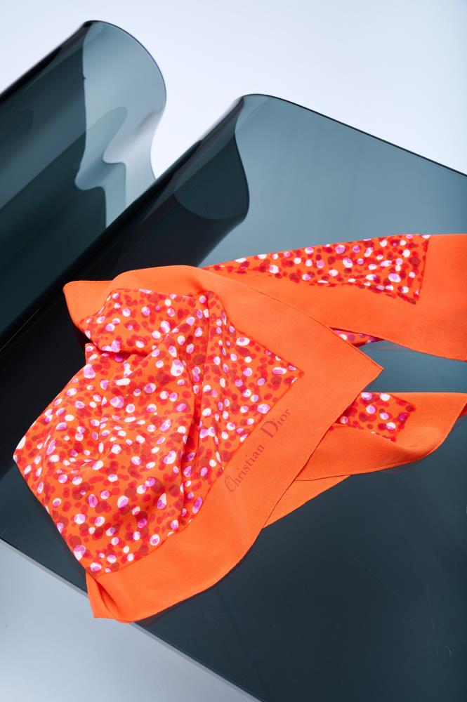 A bright orange silk scarf with violet and white dots, displayed on a flat surface.