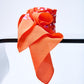 Artistic display of a premium orange designer scarf, showcasing the fluid drape and soft texture of the silk fabric alongside an intricate multicolored confetti pattern