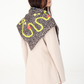 Back three-quarter perspective portrait showing a dark brown patterned silk and viscose scarf with yellow lemons and red lobsters draped triangularly over a light beige blazer, paired with blue-grey denim trousers, seen from the side-rear on a white studio background