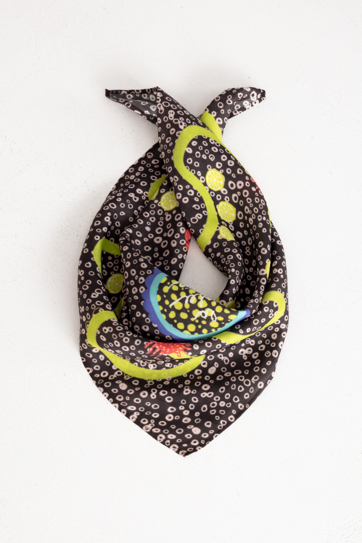 Flat lay product display of the "La Dolce Vita" dark brown silk neck scarf, elegantly folded into a triangle shape featuring vibrant yellow lemon slices, red lobsters, and colorful accents on a textured white surface