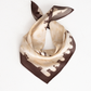 A square silk scarf with a beige and brown horse pattern, tied in a knot on a plain white background.