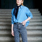 A model wearing a light blue denim shirt and grey jeans, styled with a knotted navy blue silk neck scarf for a classic, sophisticated everyday look.