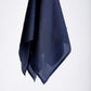 A dark blue silk scarf, partially transparent, hangs elegantly against a plain white background. The fabric drapes smoothly, creating a minimalist and serene tone.